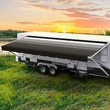 Travel trailer parked on grass at sunset with a striped patio awning fully extended