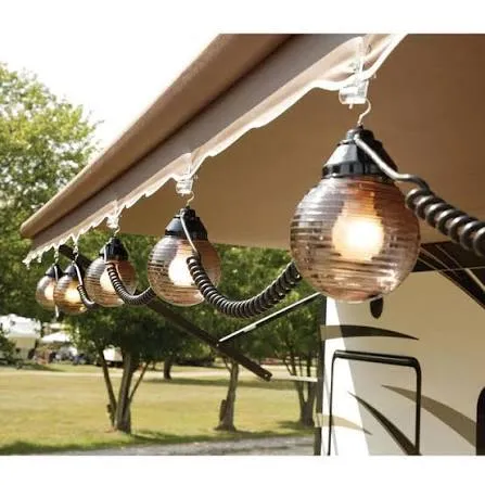 Globe string lights hanging from an RV awning's roller bar at a campground