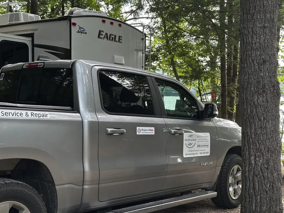 Jules RV Awnings mobile service truck parked beside a fifth-wheel trailer at a lakeside campsite, its door decal advertising RV awning installs and repairs